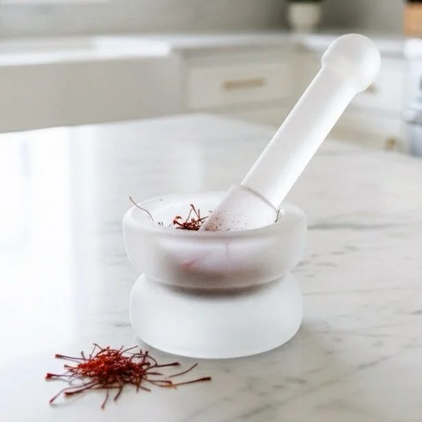 Crystal mortar and pestle with saffron strands on a marble surface.