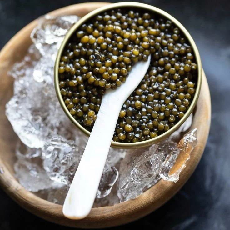 A mother-of-pearl spoon in a tin of caviar served on ice.